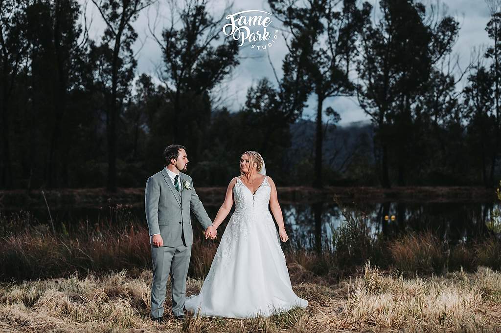 The newlyweds holding their hands and standing beside the lake at The Turpentine Tree