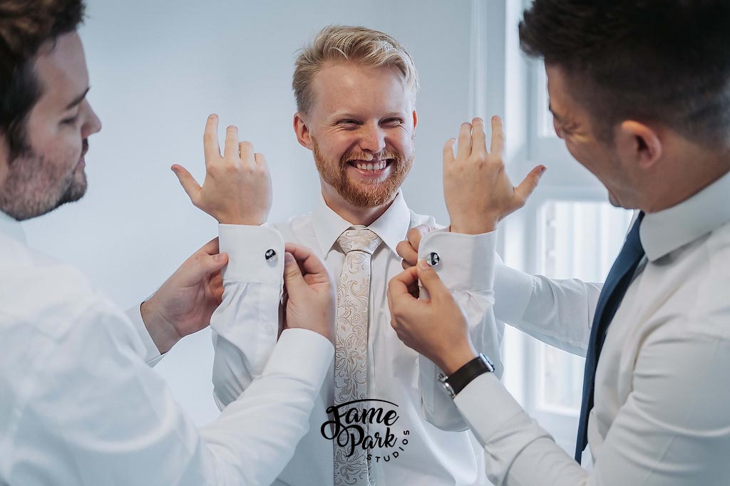 The groom is putting on his cufflink with the help of his groomsmen