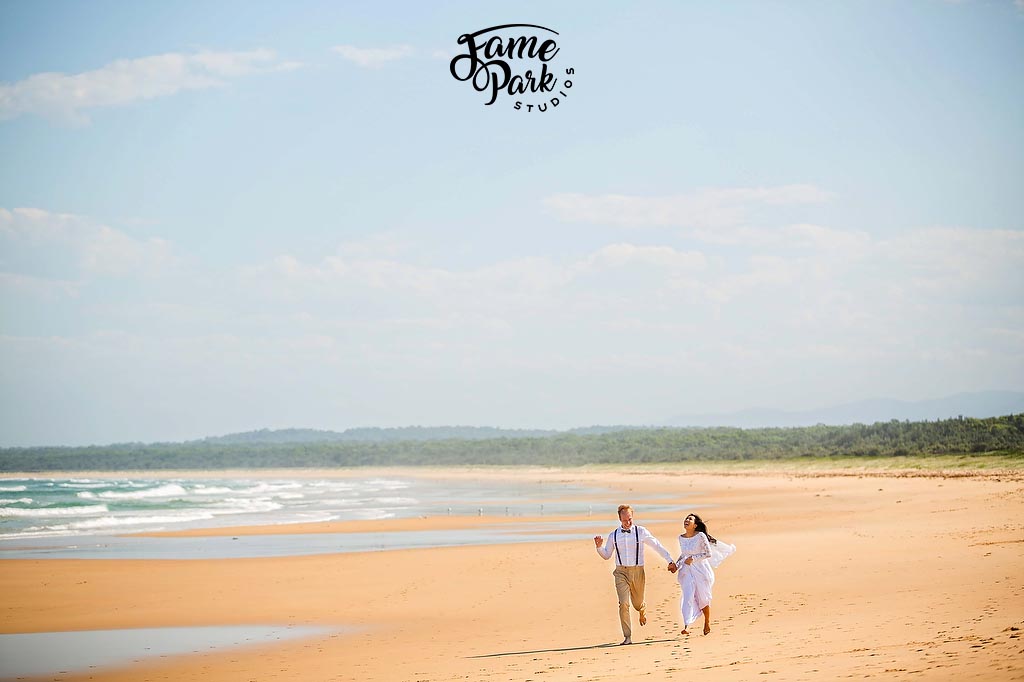 The bride and groom is holding hands and running on a beach