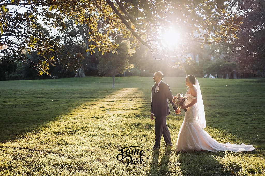 The couple is walking in front of a large tree during the sunset hours.