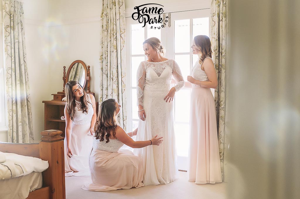 The bride is putting on her boho wedding dress with the help from her bridesmaids