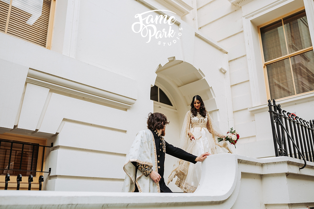 The Indian bride and groom have their photoshoot in front of a white building.