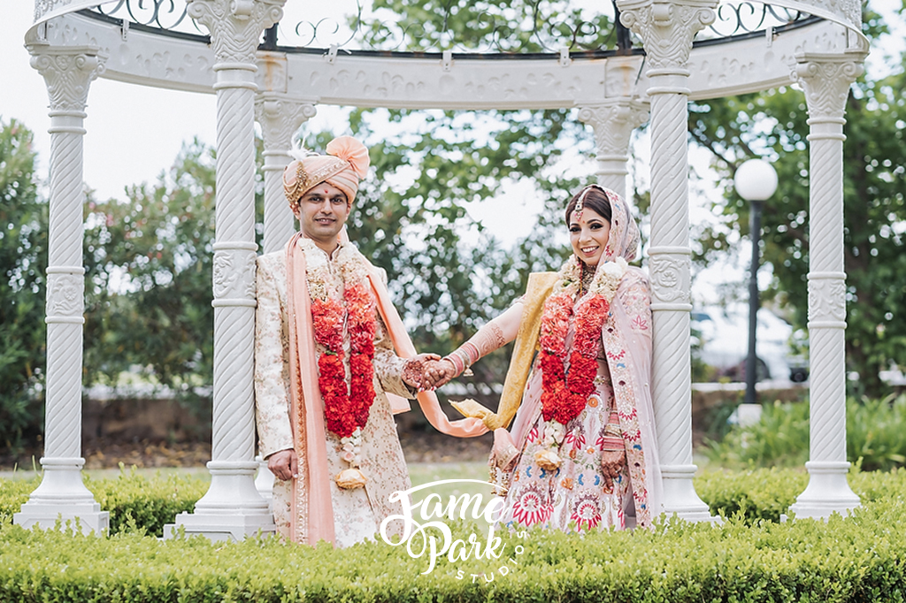 The Indian bride and groom are standing side by side and looking into the camera.