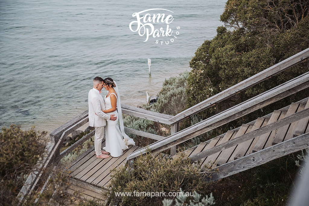The bride and groom stand face to face in a background of ocean