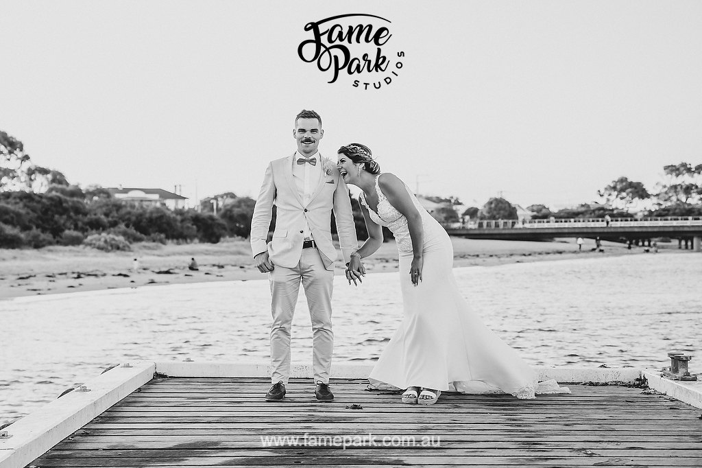 A black and white photo of newlyweds laughing out loud on a jetty