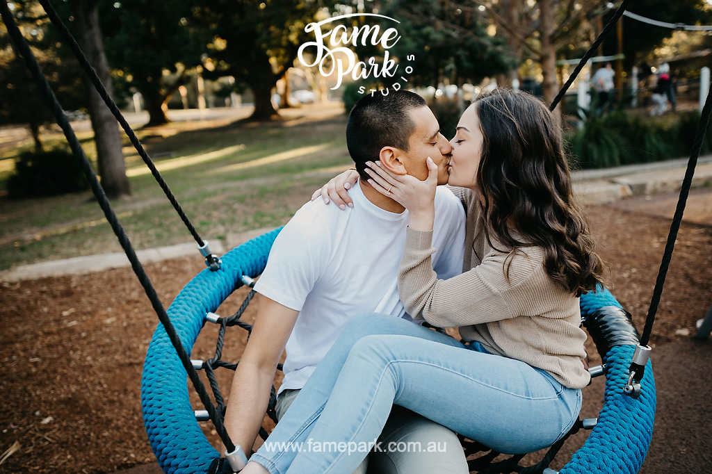 The young couple kissing on a swing in a park