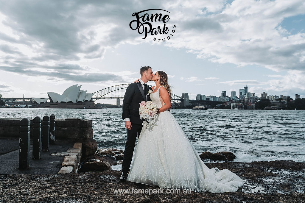 The bride and groom kissing in a background of opera house and sydney harbour bridge