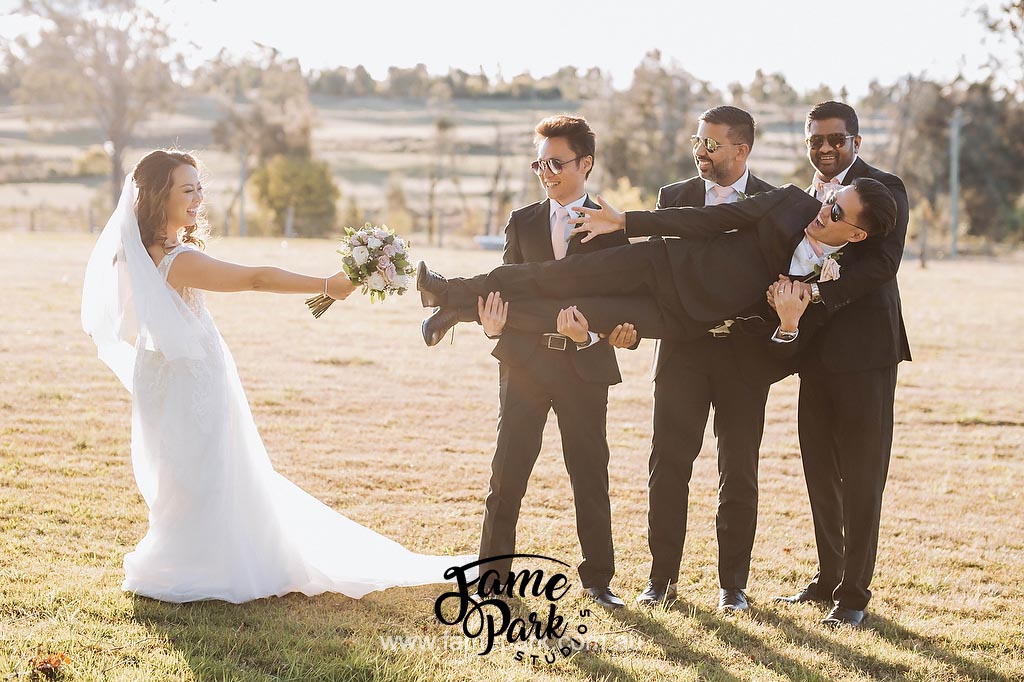 The groomsmen lift the groom high in the air, creating a playful moment that fills the scene with laughter and camaraderie, while the bride's contagious laughter adds to the joyous atmosphere.