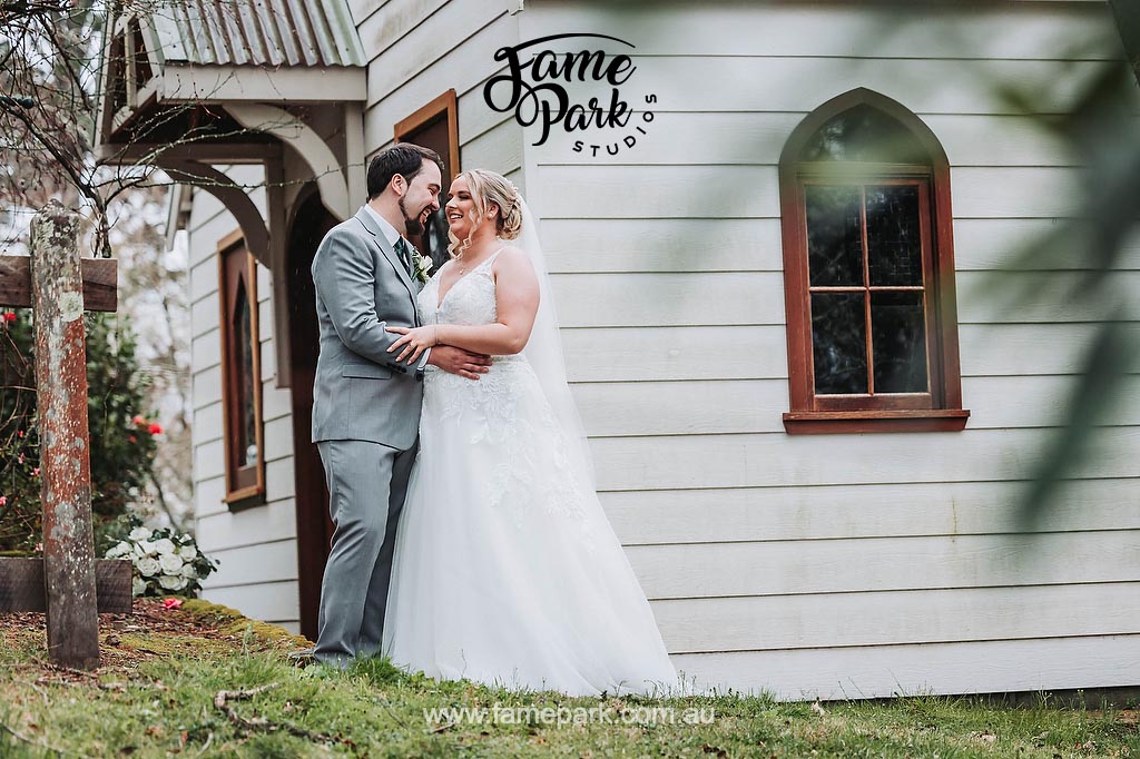 The bride and groom stand in front of a charming chapel, gazing into each other's eyes with deep love and affection, as if the world around them fades away, leaving only their connection and the promise of their union.