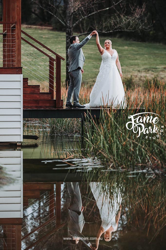 The bride and groom dance gracefully beside a serene lake, their movements mirroring the tranquility of the water, as they revel in the joy of the moment, surrounded by natural beauty.