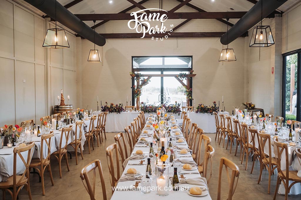A rustic-inspired reception hall adorned with charming wooden centerpieces, soft candlelight, and burlap table runners, evoking a cozy and vintage atmosphere.