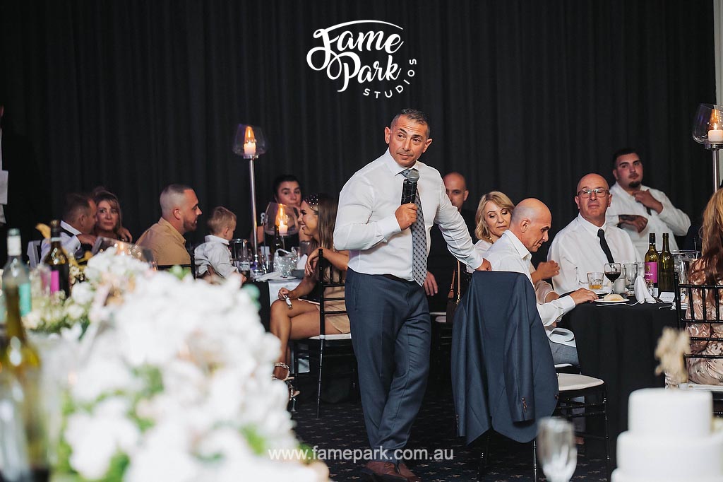 The bride's father stands before the guests, his warm smile and proud gaze capturing the room's attention as he delivers a heartfelt and touching speech, sharing cherished memories and words of love.