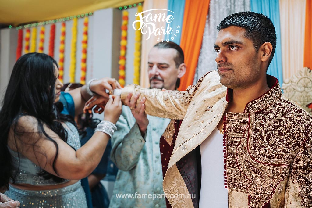 A man is wearing his Indian male wedding attire with the help of his parents.