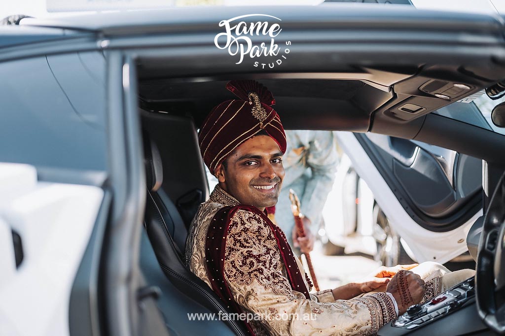 A man in traditional Indian mens wedding clothing sitting in the driver's seat of a supercar.