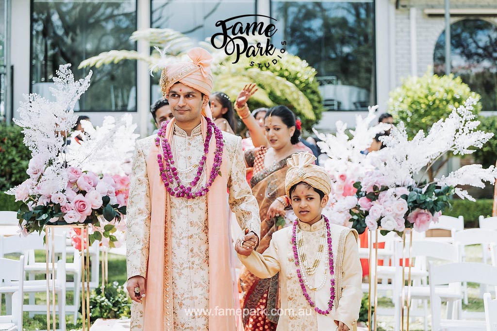 A man and his pageboy showcasing their elegant mens Indian wedding outfits during an Indian wedding procession.