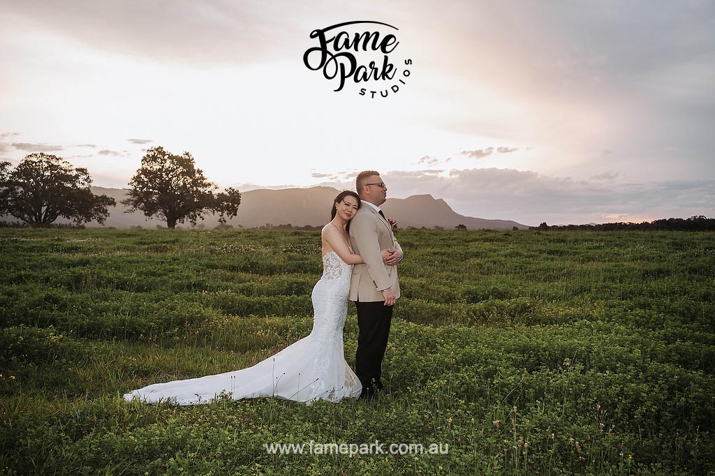 a bride and groom standing in a open field at sunset.