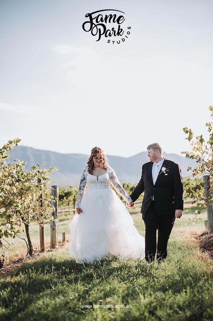 Bride and groom strolling through a Hunter Valley vineyard with majestic mountains as the backdrop for their wedding reception.