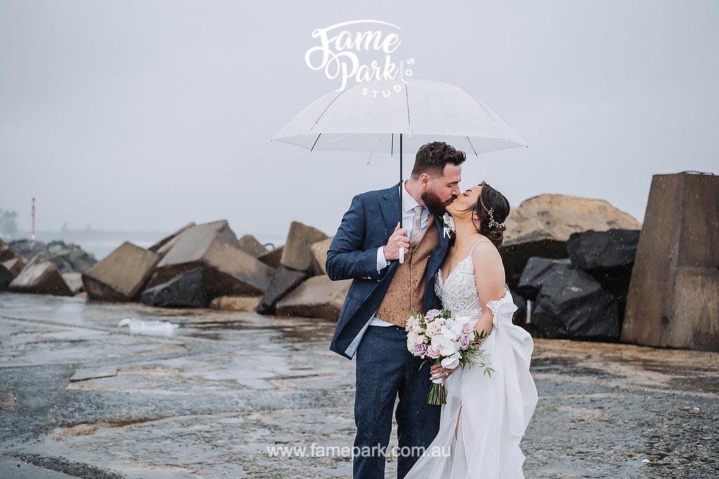 A bride and groom kiss under an umbrella near Wollongong lighthouse