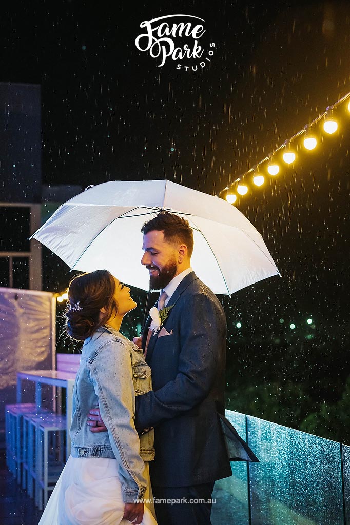 A bride and groom embrace under an umbrella at Wollongong City Beach Function Centre.