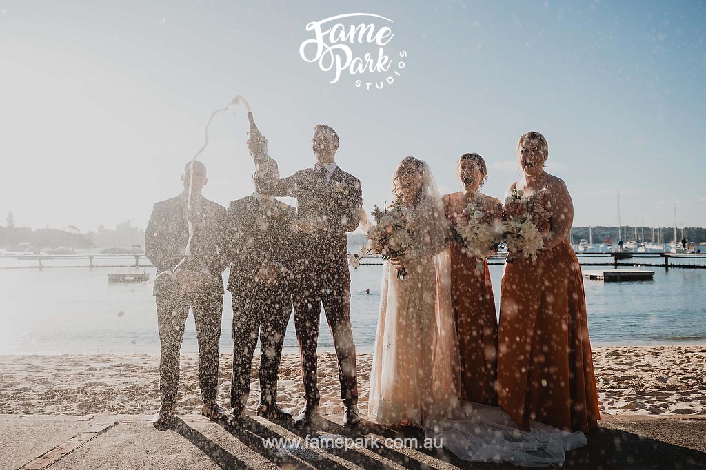 The bridal party have their champagne pop on the beach